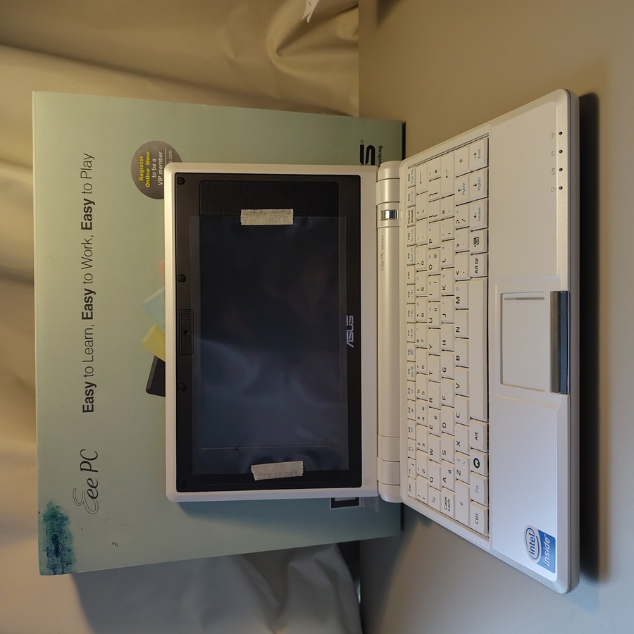 Eee PC with lid open and
    protective cover on screen. behind it, its original box